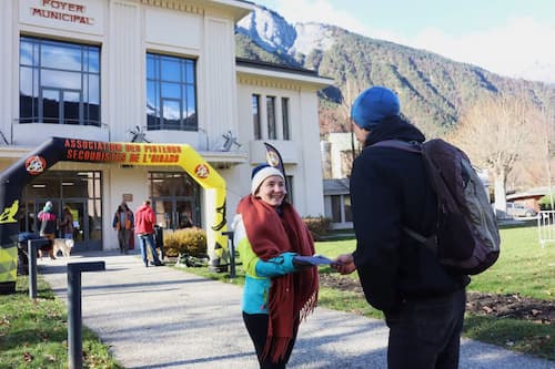 Une personne donne un tract à une autre personne devant le Foyer Municipal de Bourg d'Oisans
